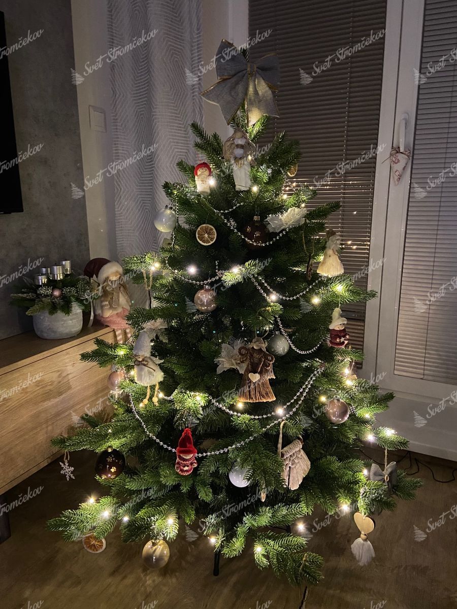 Umelý vianočný stromček 3D Smrek Exkluzívny 120cm ozdobený bielymi mašľami, sušeným ovocím a figúrkami. Na špici stromčeka je mašľa.