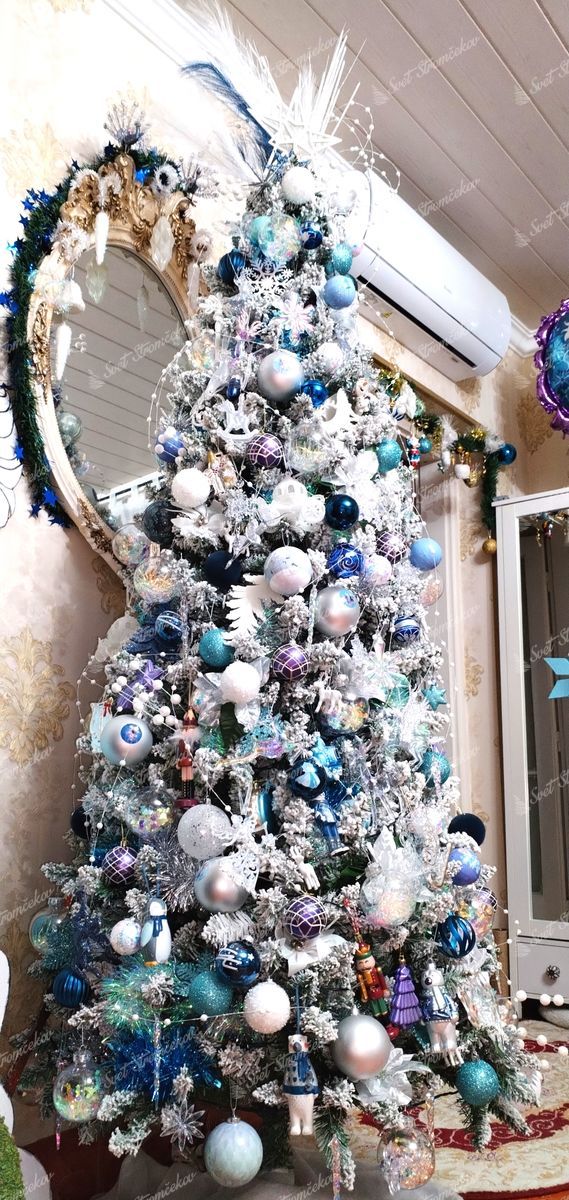 Umelý vianočný stromček Smrek Biely Úzky 210cm je husto ozdobený bielymi, modrými a striebornými ozdobami.