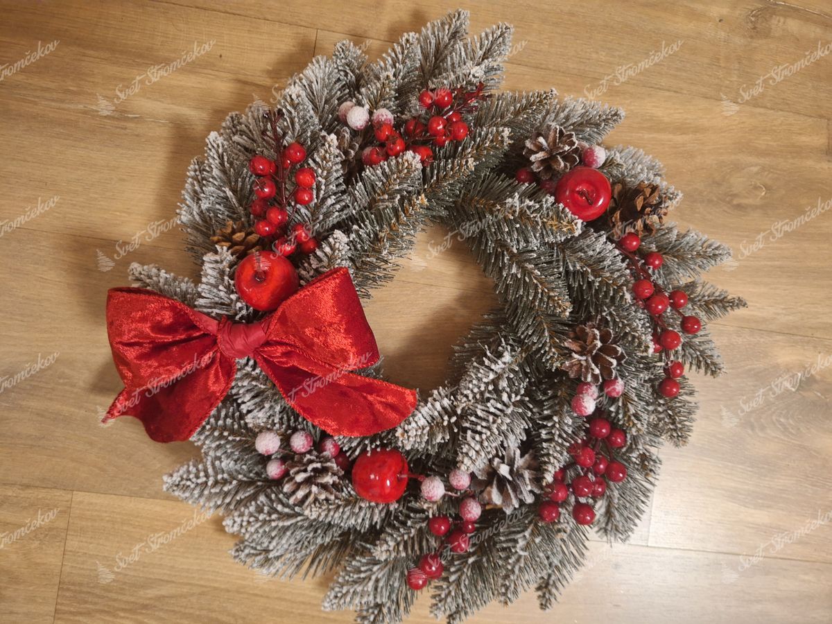 Vianočný veniec Smrek Kryštálový 50cm má vetvičky jemne posiaté snehom a doplnené šišakmi a červenými plodmi. Je ozdobený červenou mašľou.